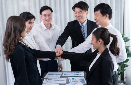 Foto de Closeup business team of suit-clad businessmen and women join hand stack together and form circle. Colleague collaborate and work together to promote harmony and teamwork concept in office workplace. - Imagen libre de derechos