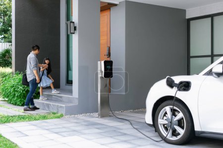 Foto de Progressive father and daughter plugs EV charger from home charging station to electric vehicle. Future eco-friendly car with EV cars powered by renewable source of clean energy. - Imagen libre de derechos