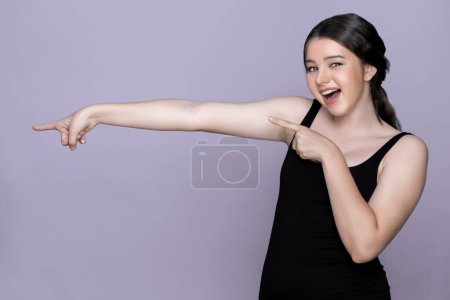 Young charming caucasian teenager girl with clean and fresh skin posing pointing fingers on empty background for beauty advertising. Cute smiling expression. Present beauty skincare cosmetic product.