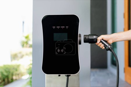 Closeup hand insert EV charger plug, green energy-powered charging point concept for EV car connected to progressive home charging station garage. Eco friendly rechargeable car.