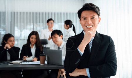 Portrait of focus young successful confident male manager, executive wearing business wear in harmony office arm crossed with blurred meeting background of colleagues, office worker.