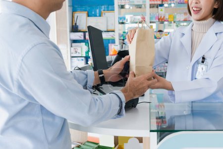 Closeup affable pharmacist give or handing customer a bag of qualified medications or medical supply, customer service concept in pharmacy. Pharmacist talking to customer in drugstore counter.