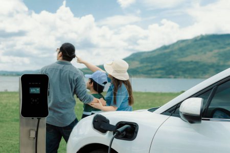 Photo for Concept of progressive happy family enjoying their time at green field and lake with electric vehicle. Electric vehicle driven by clean renewable from eco-friendly power sauce. - Royalty Free Image