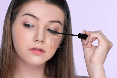 Foto de Closeup portrait of young charming applying makeup eyeshadow on her face with brush, mascara with flawless smooth skin for beauty concept. - Imagen libre de derechos