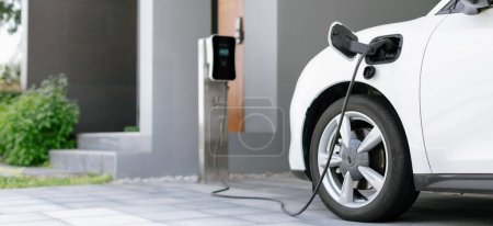 Foto de Progressive concept of EV car and home charging station powered by sustainable and clean energy with zero CO2 emission for green environmental. Charging point at residential area for electric vehicle. - Imagen libre de derechos