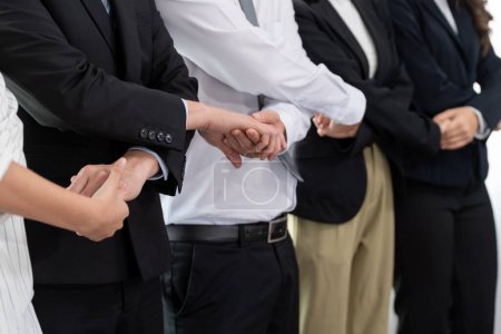 Foto de Closeup cohesive group of businesspeople standing holding hand in line together after meeting to promote harmony in workplace. Asian office workers strong teamwork and unity concept. - Imagen libre de derechos