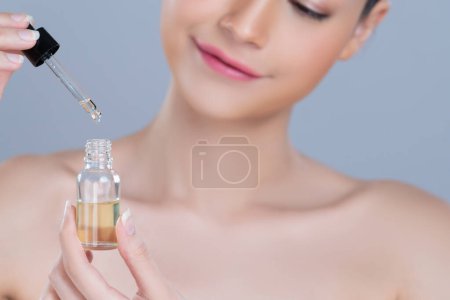Photo for Focus cannabis extracted oil bottle with dropper lid holding by blurred glamorous beautiful asian woman with perfect clean skin and soft smooth makeup in isolated background. - Royalty Free Image