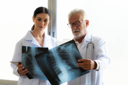 In einem sterilen Krankenhauszimmer halten und untersuchen zwei professionelle Röntgenspezialisten eine Röntgenaufnahme zur medizinischen Röntgendiagnostik. Arztneuling sucht Rat bei Krankheit des Patienten bei erfahrenem älteren Arzt.