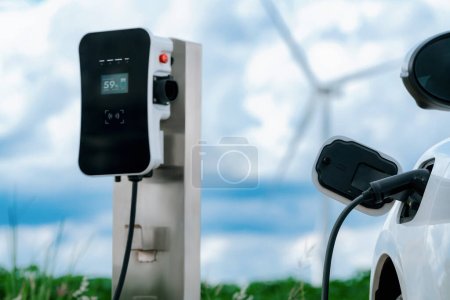 Photo for Progressive combination of wind turbine and EV car, future energy infrastructure. Electric vehicle being charged at charging station powered by renewable energy from wind turbine in the countryside. - Royalty Free Image