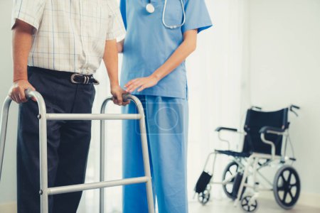 Téléchargez les photos : Physiotherapist assists contented senior man on folding walker. Recuperation for elderly, seniors care, nursing home. - en image libre de droit