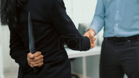 Foto de Back view of businesswoman shaking hands with another businessman while holding a knife behind his back. Concept of back backstabbing in business, backstabbing between colleagues. - Imagen libre de derechos