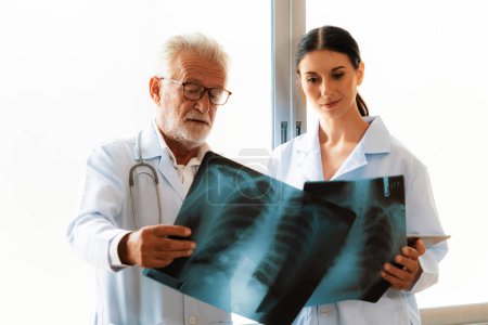 En una sala estéril del hospital, dos radiografos profesionales sostienen y examinan una radiografía para el diagnóstico médico de rayos X. El médico novato busca consejo sobre una condición de los pacientes de un médico experimentado.