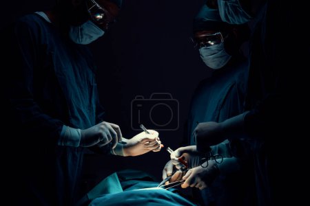 Foto de Equipo quirúrgico realizando cirugía al paciente en quirófano estéril. En una sala de cirugía iluminada por una lámpara, un equipo quirúrgico profesional y seguro proporciona atención médica a un paciente inconsciente. - Imagen libre de derechos
