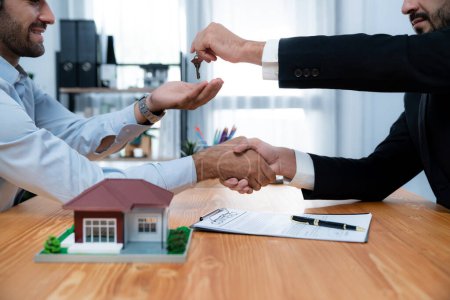 Closeup real estate broker or landlord shake hand with buyer and give a key. Client agree on house loan contract terms. Successful home purchasing deal with real estate agent in office. Fervent