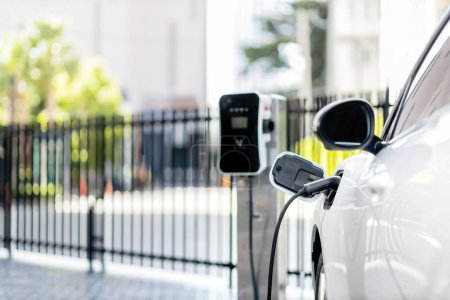 Photo for Focus closeup electric vehicle plugged in with EV charger device from blurred background of public charging station powered by renewable clean energy for progressive eco-friendly car concept. - Royalty Free Image