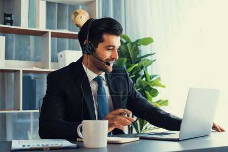Photo for Male call center operator or telesales representative siting at his office desk wearing headset and engaged in conversation with client providing customer service support or making a sale. fervent - Royalty Free Image