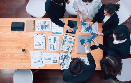 Foto de Top view businesspeople and colleagues in formal wear putting jigsaw puzzles together over meeting table with financial report papers in harmony office for team building concept. - Imagen libre de derechos