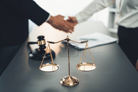 Focus gavel and justice scale on blur background of lawyer colleagues handshake after successful legal deal for lawsuit to advocate resolves dispute in court ensuring trustworthy partner. Equilibrium