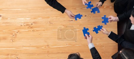 Top view businesspeople and colleagues in formal wear putting jigsaw puzzles together over meeting table with financial report papers in harmony office for team building concept.