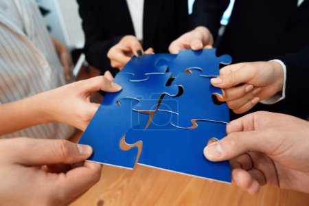Foto de Closeup top view business team of office worker putting jigsaw puzzle together over table filled with financial report paper in workplace with manager to promote harmony concept in meeting room. - Imagen libre de derechos