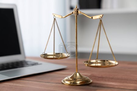 Symbolisiert Gerechtigkeit und rechtliche Autorität, goldene Waage auf dem Schreibtisch mit Laptop im Hintergrund der Anwaltskanzlei, die das Konzept der Gleichheit und des fairen Urteils von Anwälten und Richtern widerspiegelt. Gleichgewicht