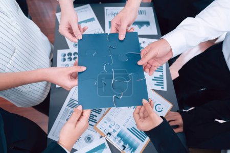 Foto de Closeup top view business team of office worker putting jigsaw puzzle together over table filled with financial report paper in workplace with manager to promote harmony concept in meeting room. - Imagen libre de derechos