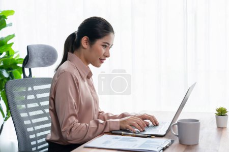 Young asian businesswoman is working and taking notes in her modern office workspace with cup of coffee in her hand, demonstrating professionalism as attractive and diligent office lady. Enthusiastic