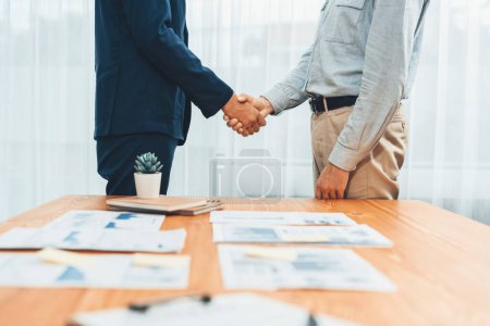 Photo for Two businesspeople shake hand after signing contract document to merge their partnerships in conference room and finalized pile of papers of financial report and data analysis on meeting table. Entity - Royalty Free Image