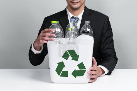 Businessman hold recycle bin filled with plastic bottle on isolated background. Corporate responsibility for green environment and community. Waste separation and management concept. Alter