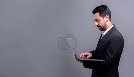 Homme d'affaires réussi en costume noir avec concept technologique innovant, pose debout et tenant ordinateur portable et souriant avec excitation sur fond de copyspace pour la promotion ou la publicité. Fervent