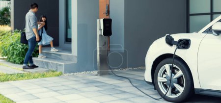 Foto de Progressive father and daughter plugs EV charger from home charging station to electric vehicle. Future eco-friendly car with EV cars powered by renewable source of clean energy. - Imagen libre de derechos