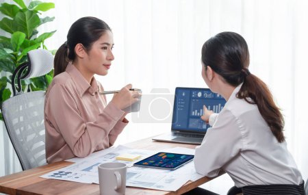 Analyst team colleague discuss financial data on digital dashboard, analyzing charts graph display on laptop and tablet screen. Modern office use business intelligence to plan marketing. Enthusiastic
