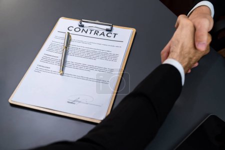 Focus business contract paper with blur background of handshake after successfully close business deal, sealing partnership agreement. Legal document and handshaking as formal agreement. Fervent