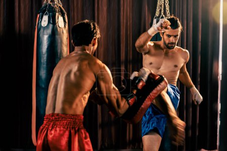 Photo for Asian and Caucasian Muay Thai boxer unleash kick attack in fierce boxing training session, delivering kicking strike to sparring trainer, showcasing Muay Thai boxing technique and skill. Impetus - Royalty Free Image