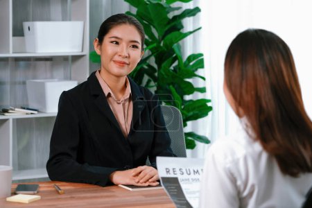 Zwei asiatische Frauen führen Vorstellungsgespräche im Büro. Die Bewerberinnen tragen formelle Anzüge, während sie über ihren Lebenslauf und ihre Bewerbung sprechen. Die Interviewer fragen positiv und gesprächig nach. Enthusiastisch