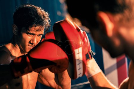Foto de El boxeador asiático y caucásico Muay Thai desata ponche en feroz sesión de entrenamiento de boxeo, entregando golpe de puñetazo al entrenador de sparring, mostrando la técnica y habilidad de boxeo Muay Thai. Impulso - Imagen libre de derechos