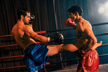 Téléchargez les photos : Le boxeur asiatique et caucasien Muay Thai lance une attaque de coups de pied dans un match de boxe féroce tandis que le concurrent en position défensive tient la jambe de coups de pied avec des prouesses de combat implacables. Impulsion - en image libre de droit