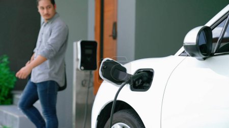 Photo for A man unplugs the electric vehicles charger at his residence. Concept of the use of electric vehicles in a progressive lifestyle contributes to a clean and healthy environment. - Royalty Free Image