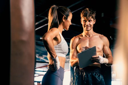 Photo for Asian female Muay Thai boxer and her personal boxing trainer discussing on her physical progress in the gym reflecting commitment to her body muscle growth and boxing performance. Impetus - Royalty Free Image