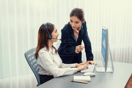 Photo for Asian female customer support operator wearing headset is guided by her supportive manager. Experienced colleague help operator handle a call with a client, providing advice and guidance. Enthusiastic - Royalty Free Image