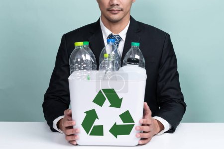 Téléchargez les photos : Un homme d'affaires tient une corbeille remplie d'une bouteille en plastique sur fond isolé. Responsabilité de l'entreprise pour l'environnement vert et la communauté. Concept de séparation et de gestion des déchets. Modifier - en image libre de droit