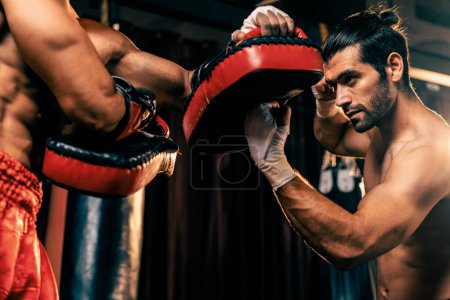 Téléchargez les photos : Le boxeur asiatique et caucasien Muay Thai déclenche une attaque de poinçon de coupe supérieure dans une séance d'entraînement de boxe féroce, livre une frappe de poinçon à l'entraîneur sparring, mettant en valeur la technique et les compétences de boxe thaïlandaise Muay. Impulsion - en image libre de droit