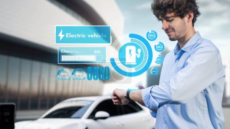 Photo for Businessman check EV car battery status on smartwatch hologram while recharge from charging station with modern building background. Futuristic lifestyle of clean energy for EV tech adaptation. Peruse - Royalty Free Image