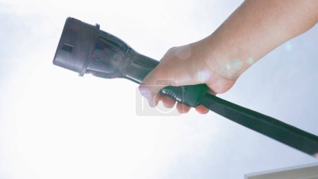 Photo for Closeup hand grasping an EV plug for electric vehicle with the midday sky in the background as progressive idea of alternative sustainable clean and green energy for environmental concern. - Royalty Free Image