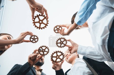 Photo for Below view office worker holding cog wheel as unity and teamwork in corporate workplace concept. Diverse colleague business people as symbol of visionary system teamwork for business success. Concord - Royalty Free Image