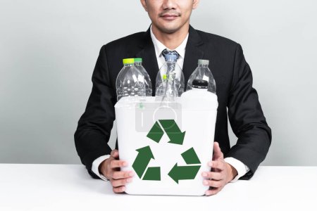 Téléchargez les photos : Un homme d'affaires tient une corbeille remplie d'une bouteille en plastique sur fond isolé. Responsabilité de l'entreprise pour l'environnement vert et la communauté. Concept de séparation et de gestion des déchets. Modifier - en image libre de droit
