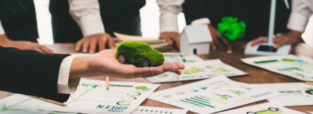 Téléchargez les photos : Homme d'affaires tenant modèle de voiture verte EV mock dans la voiture électrique réunion de l'entreprise, les gens d'affaires de planification marketing stratégique pour le produit de véhicule respectueux de l'environnement en utilisant l'énergie propre avec zéro net. - en image libre de droit