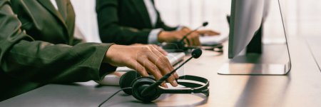 Photo for Panorama focus hand holding headset on call center workspace desk with blur background of operator team or telesales representative engaging in providing client with customer support service. Prodigy - Royalty Free Image