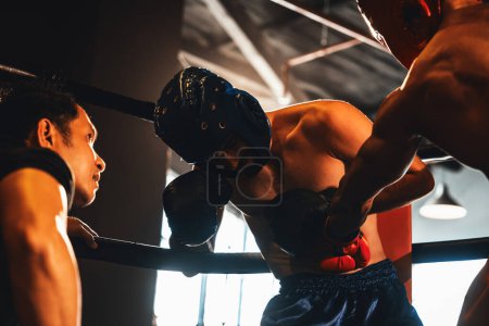 Téléchargez les photos : Combattant boxeur concurrent luttent avec douleur et désavantage sur le match de boxe sur le ring tandis que l'arbitre observer de près l'action. Boxer avec casque de sécurité essayer de se défendre. Impulsion - en image libre de droit