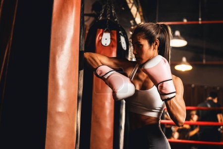 Die asiatische Muay Thai Boxerin entfesselt in einem heftigen Boxtraining eine Ellbogenattacke, indem sie Ellbogenschläge an Kickbag-Boxausrüstung abgibt und Muay Thai-Boxtechnik und -Geschick demonstriert. Impulse